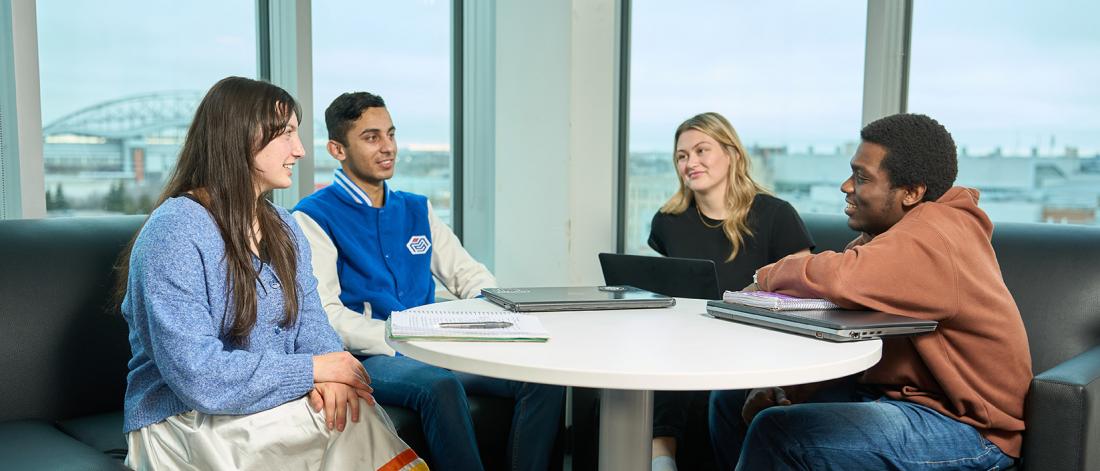 four students sit around a table chatting