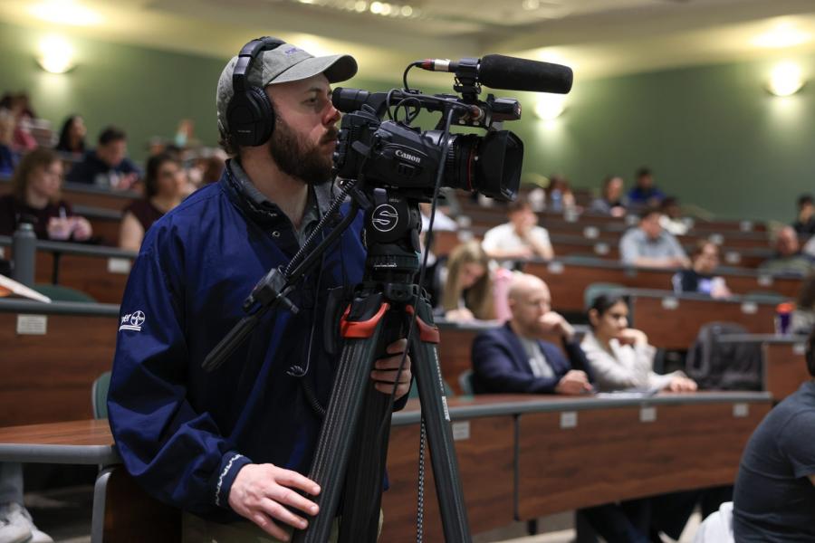 Man standing behind a video camera recording a presentation