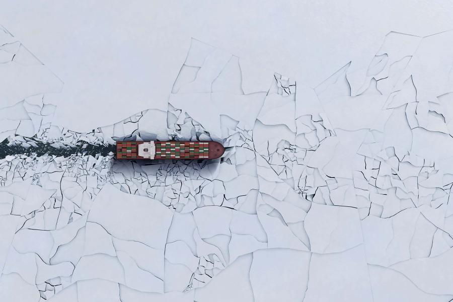 An icebreaker ship is seen from above sailing through cracked ice.