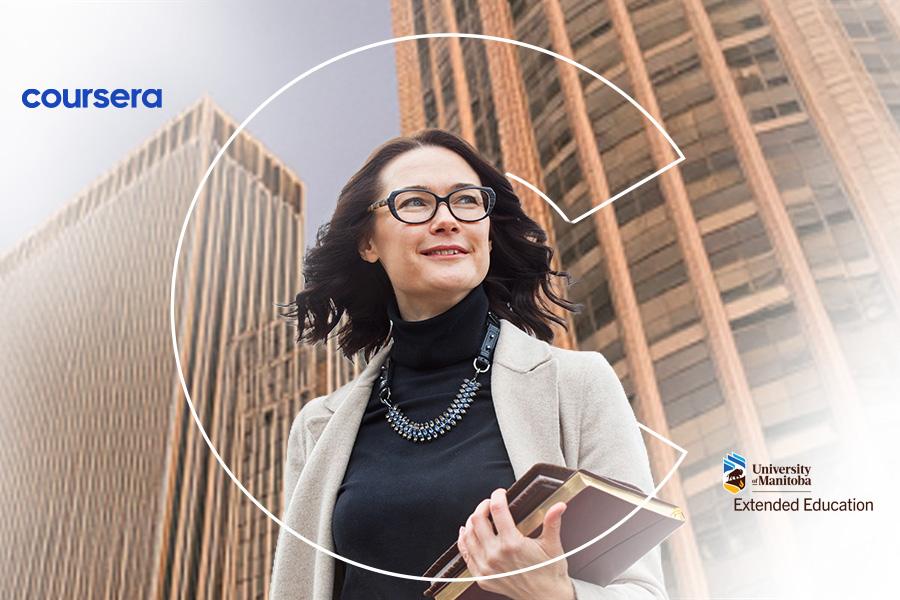 A woman wearing glasses and holding books stands in front of buildings.