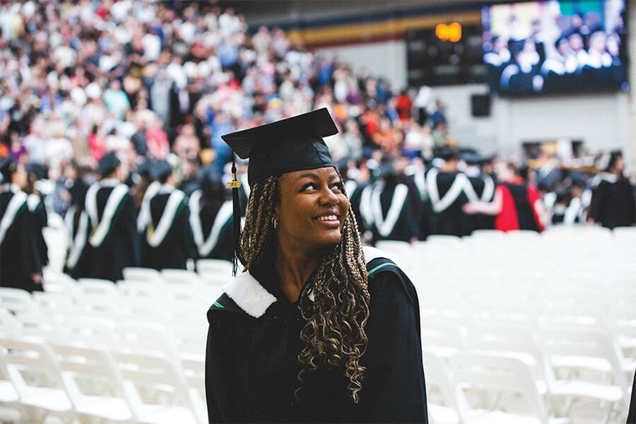 A graduating student with cap and gown smiling in a convocation hall.