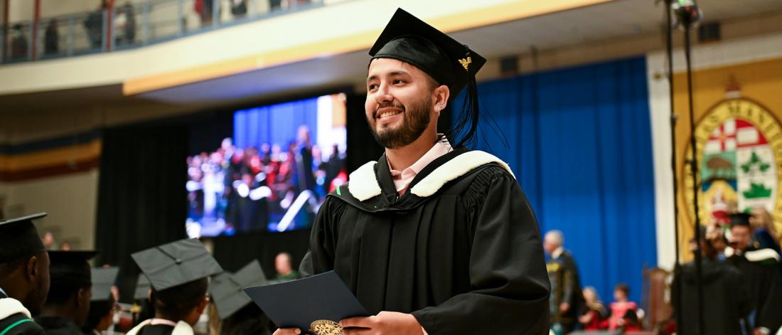 A student wearing a cap and gown holding a diploma.