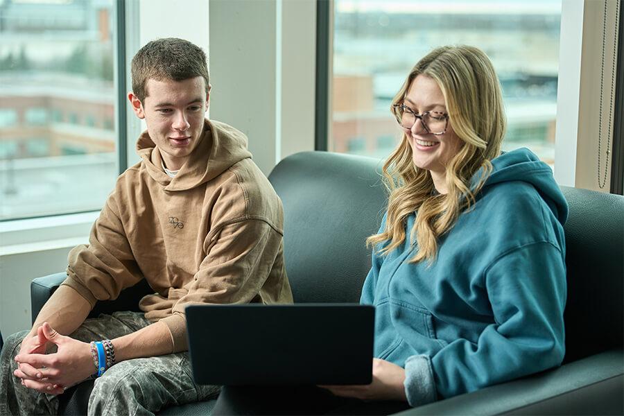 Two students in a student lounge looking at a laptop together.