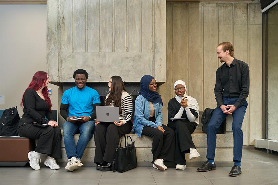 Several students sitting along a concrete bench talking to each other.