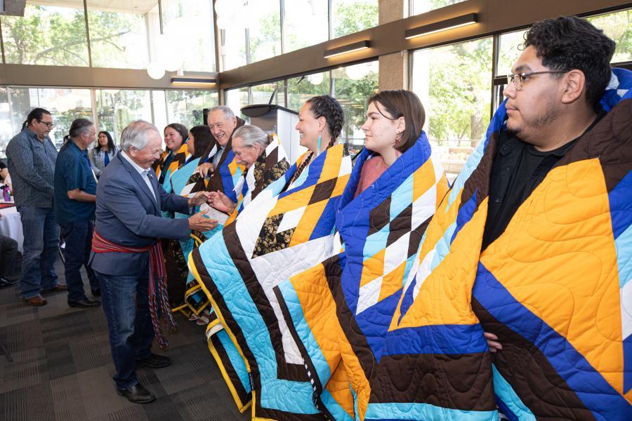 Student-honourees wrapped in star blankets stand in a line and greet community members.