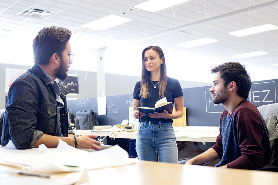 Image of two male students discussing topics with a female classmate. 