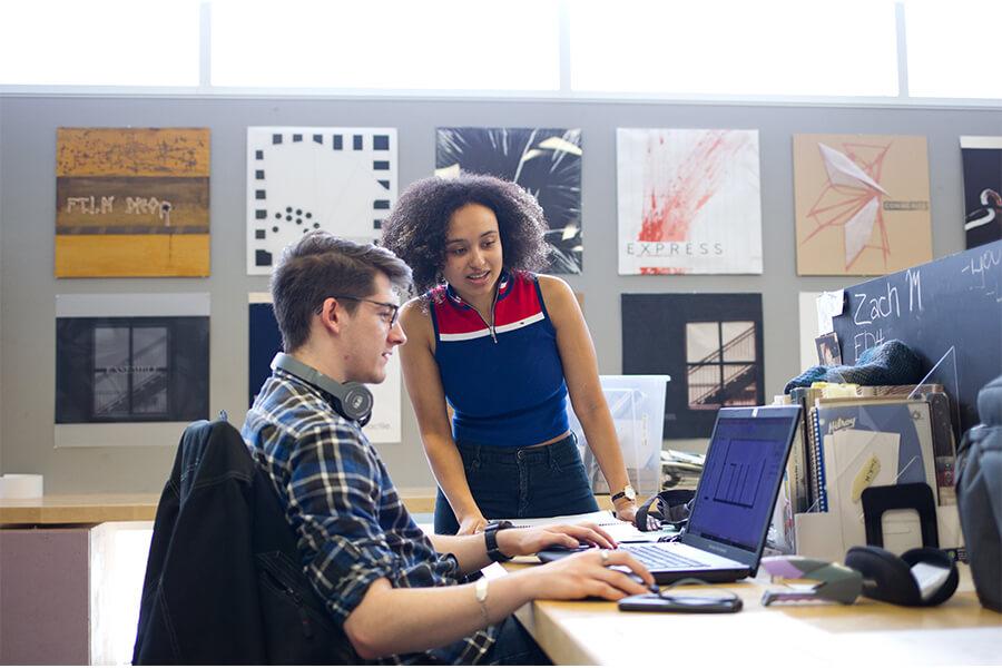 Two students in an art studio looking at a laptop.
