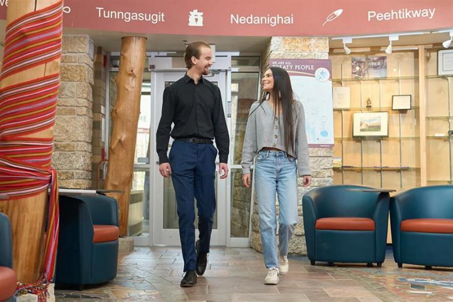 An image of two people smiling while walking into Migizii Agamik at University of Manitoba