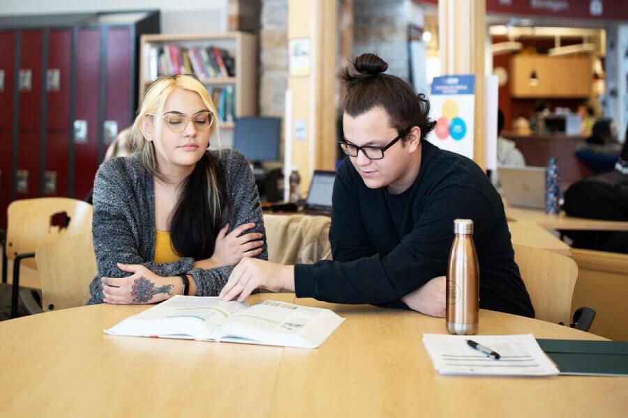 Two students sit at a table inside Migizii Agamik.