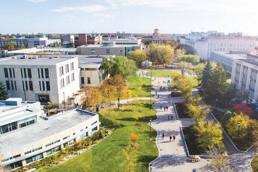 Students walk along Curry Place walkway past trees with leaves on the Fort Garry campus.