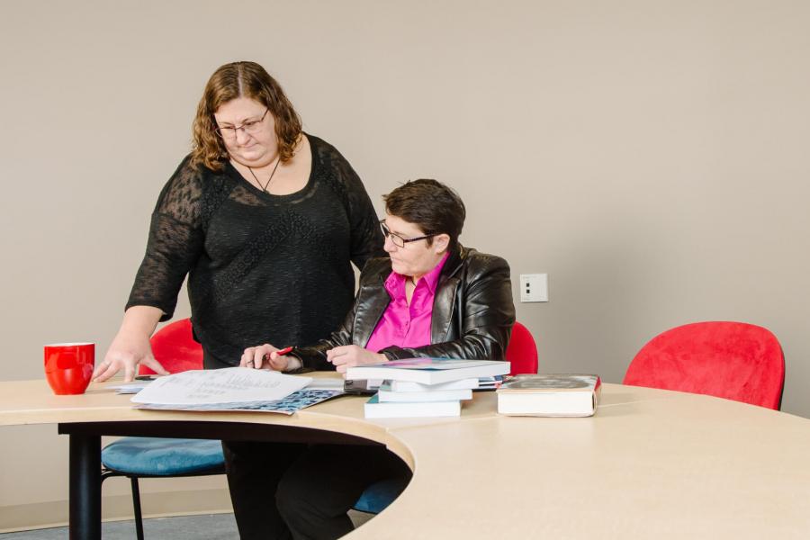Kiera Ladner and one other woman work together at a circular table inside the Mamawipawin functional community research space.
