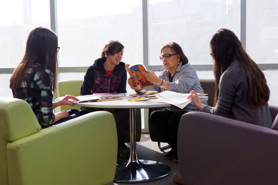 Three students sit with an Indigenous Elder studying books about Honouring Elders, medicinal wild plants and more. 
