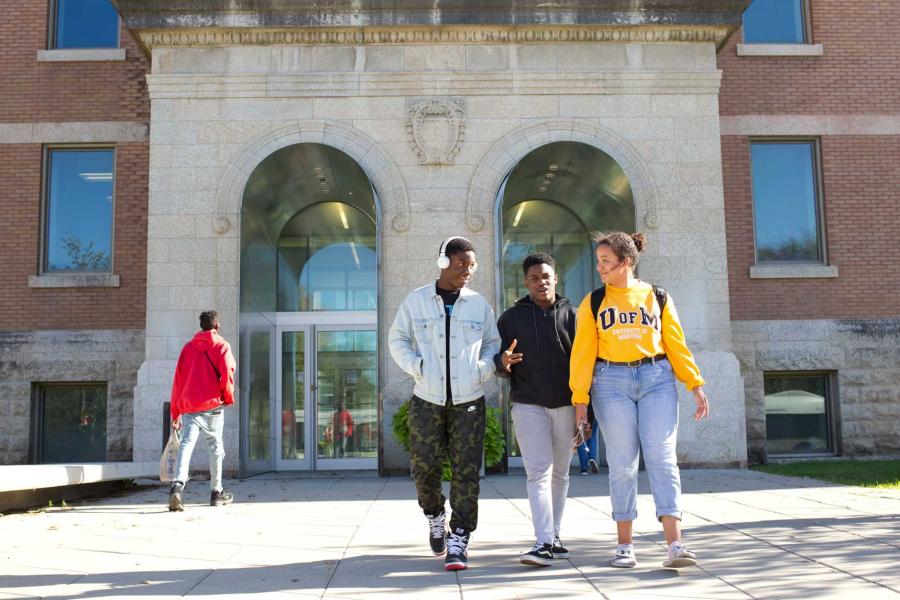 Three University of Manitoba students talking to each other, walking away from a building on campus.
