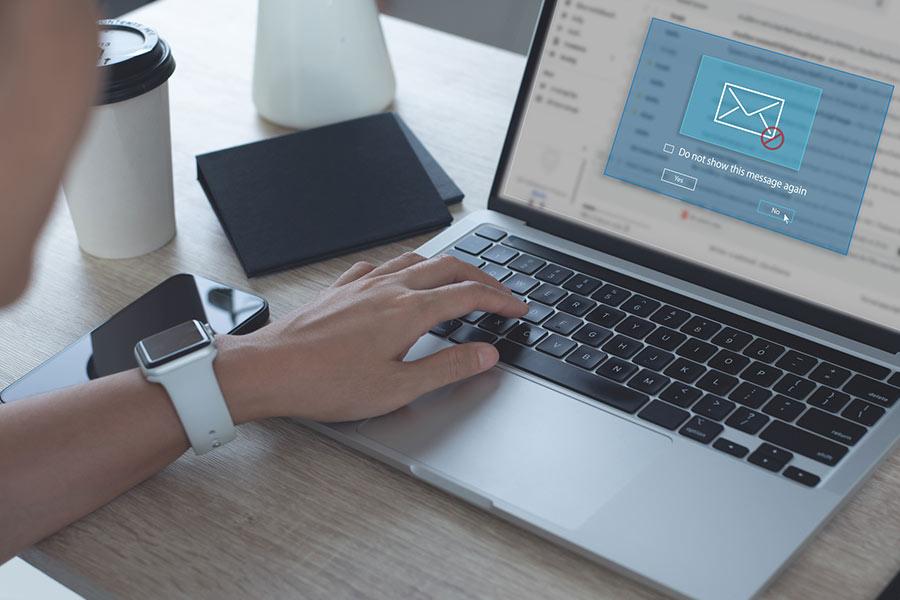 Hands at a laptop keyboard with a spam email message showing on the laptop screen