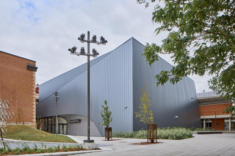 Exterior view of the Desautels Concert Hall with its distinctive angular, silver metal façade, surrounded by a landscaped plaza with trees and modern lighting.