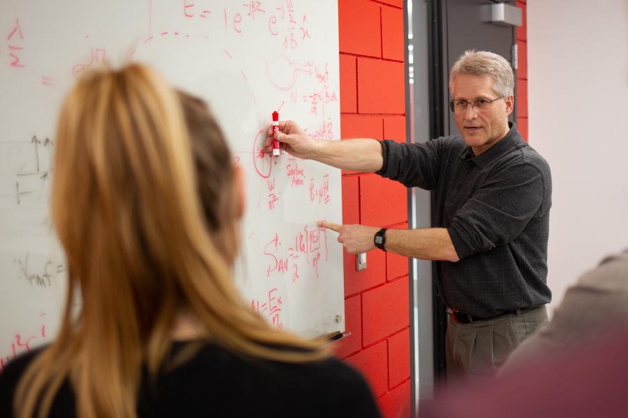 A professor instructs a student while pointing at a dry erase whiteboard.