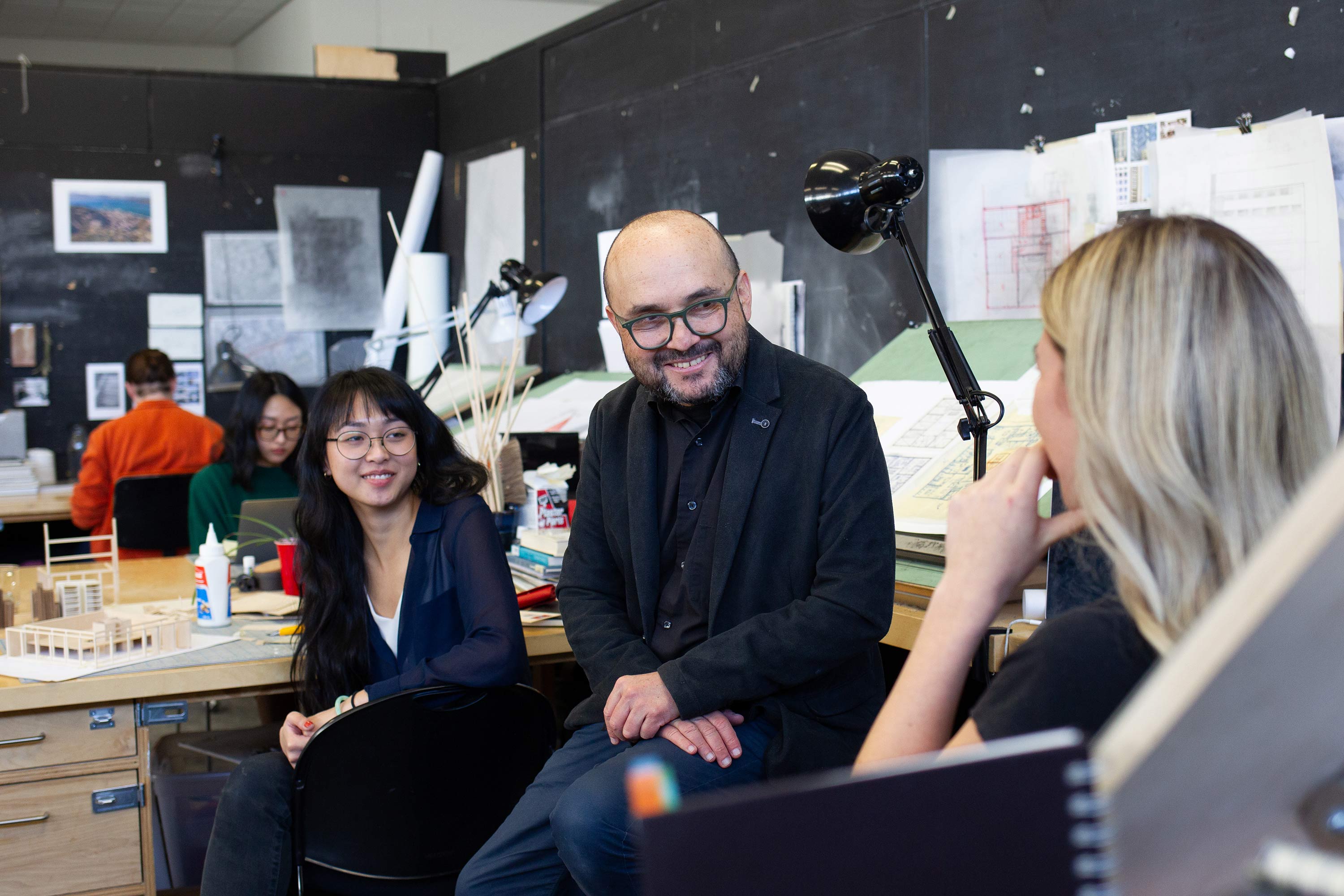 An instructor sitting with two students in a lab.