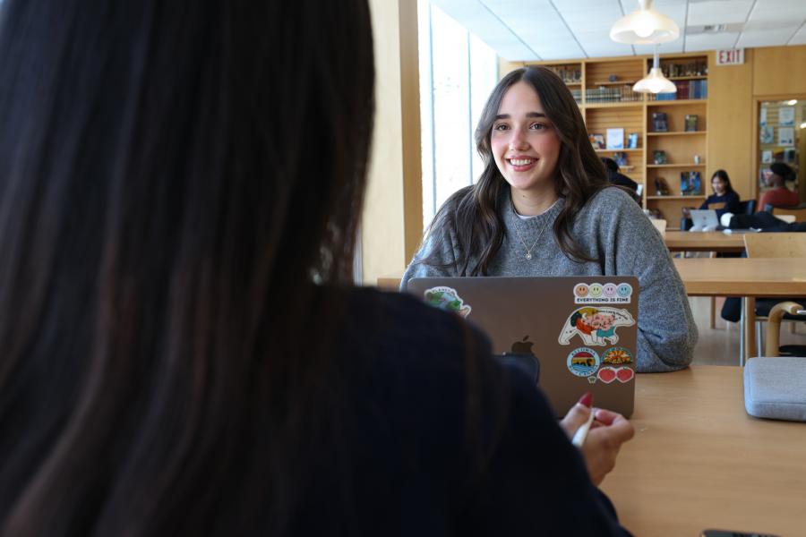 A student studying on her laptop and smiling at another student