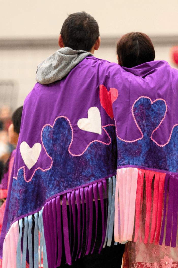 People wearing regalia walk together at a pow wow gathering.