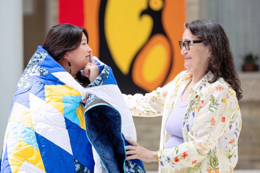 An Elder places a Star Blanket around an honouree during a HICC blanketing ceremony.