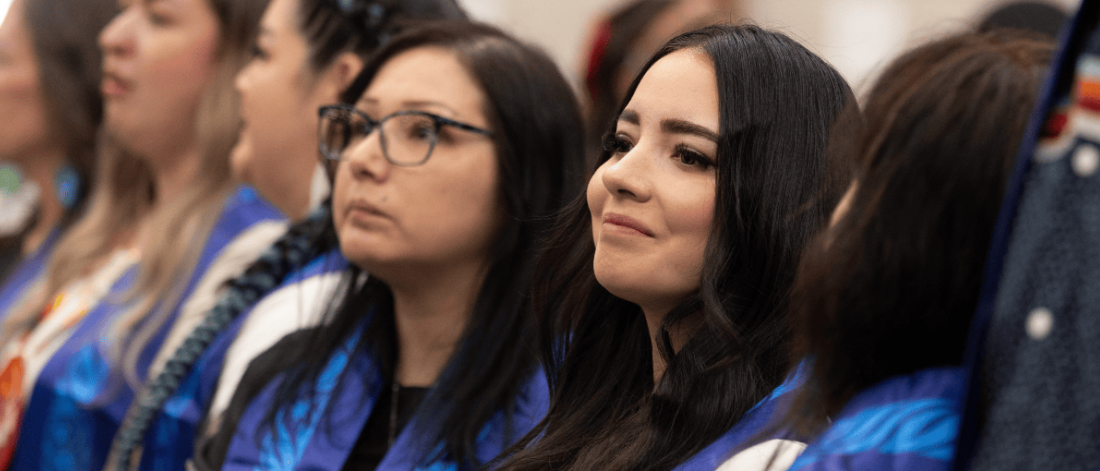 Graduates wearing blue stoles sit together during a ceremony.