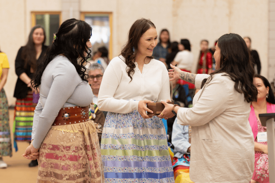 A woman receives a small gift during a Pow Wow ceremony, surrounded by others.