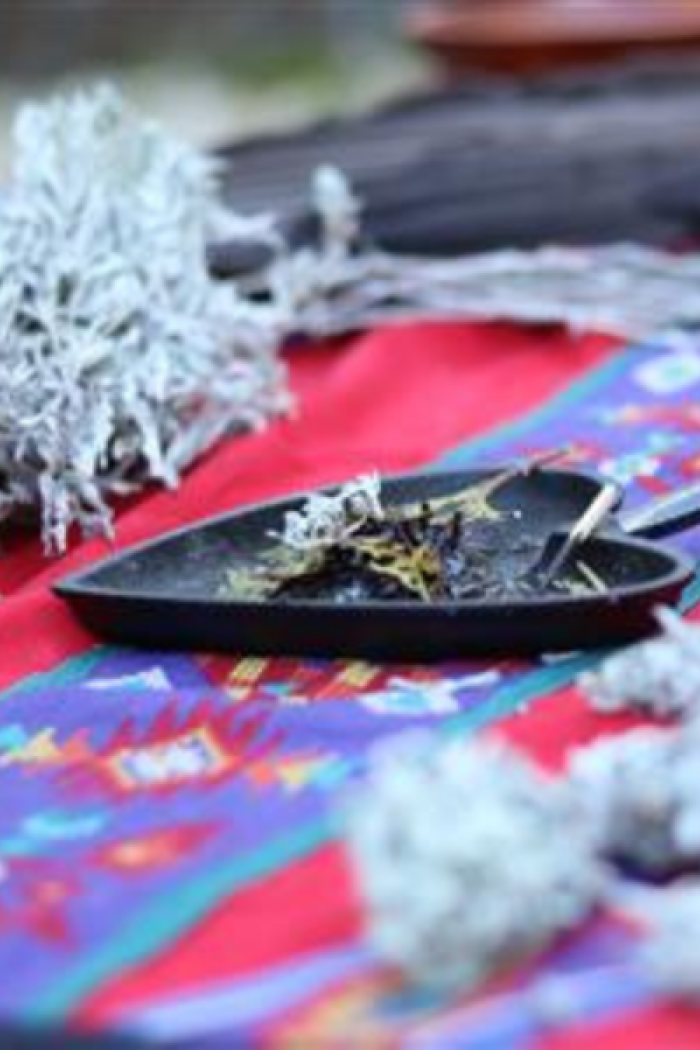 Close-up of smudging materials on a colorful cloth, including sage, a smudge pan with burning herbs, and other ceremonial items.