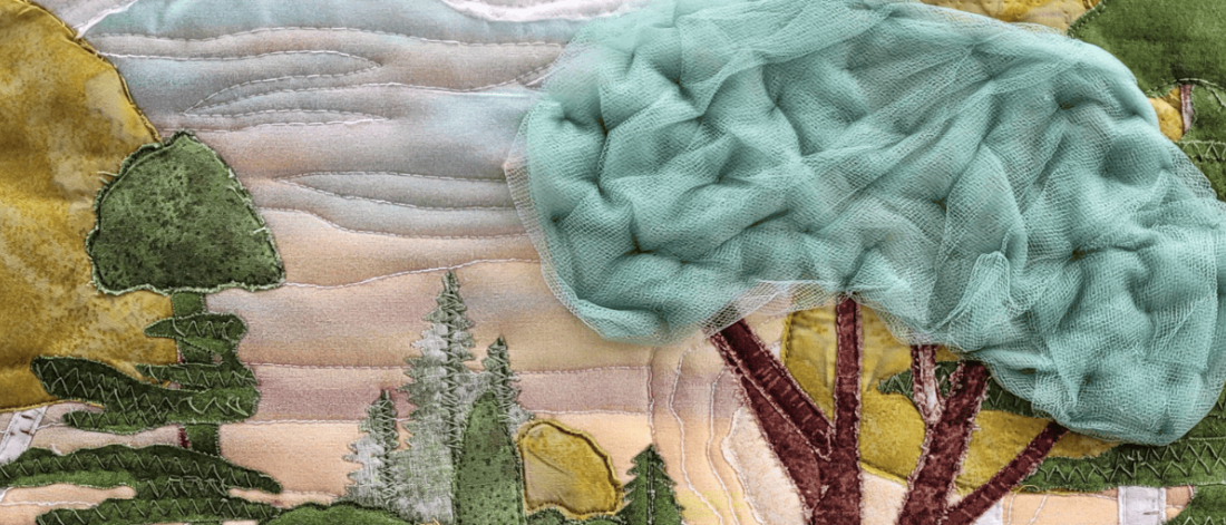 Textile artwork depicting a stylized landscape with layered fabric trees, stitched hills, and a large tree with a soft, textured green canopy.